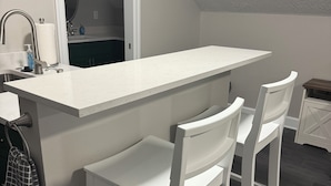 A kitchen with a white countertop, two white bar stools, a sink, and a mirror. - Moonstruck Studio: In Wine Country (Newberg)