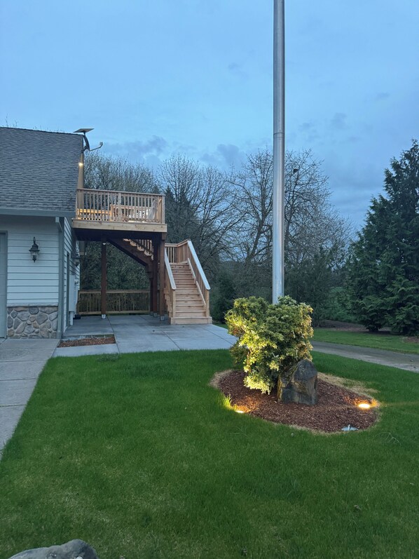 A two-story house with a wooden deck, a staircase, and a well-maintained lawn.