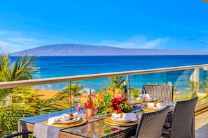 Ein Esstisch mit Geschirr, Gläsern und einer Flasche, mit Blick auf einen Strand und das Meer.