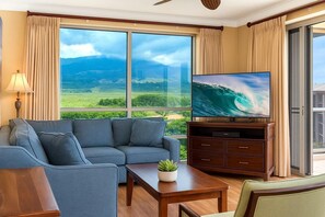 A living room with a large window, a sofa, a TV, and a small table with a plant. - Honua Kai | Ocean View 6 BR, Sleeps 20 | Car Incl. w/ 6+ Nights | HKH ML-3101 by KBM (Lahaina)