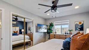 Un dormitorio con cama, cómoda, espejo, ventilador de techo y ventana.