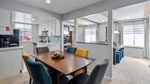 Una cocina moderna con armarios blancos, una mesa de comedor con sillas y vistas al exterior a través de amplios ventanales.