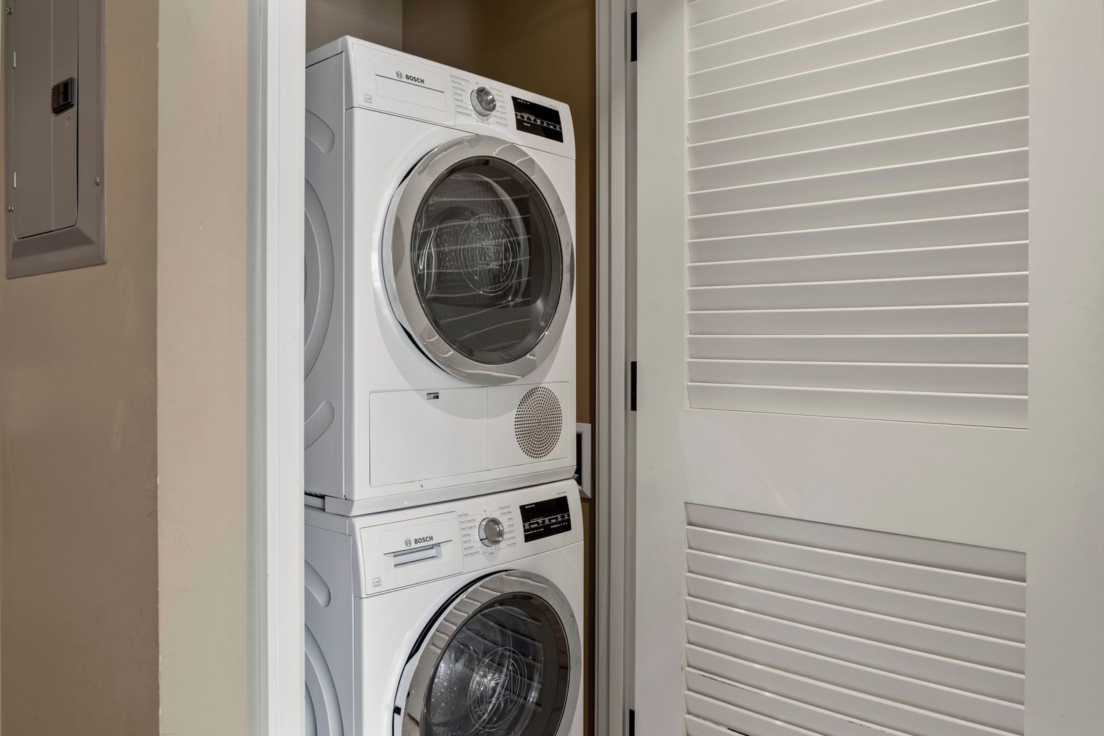 A stacked Bosch washing machine in a laundry room with a white door and blinds.