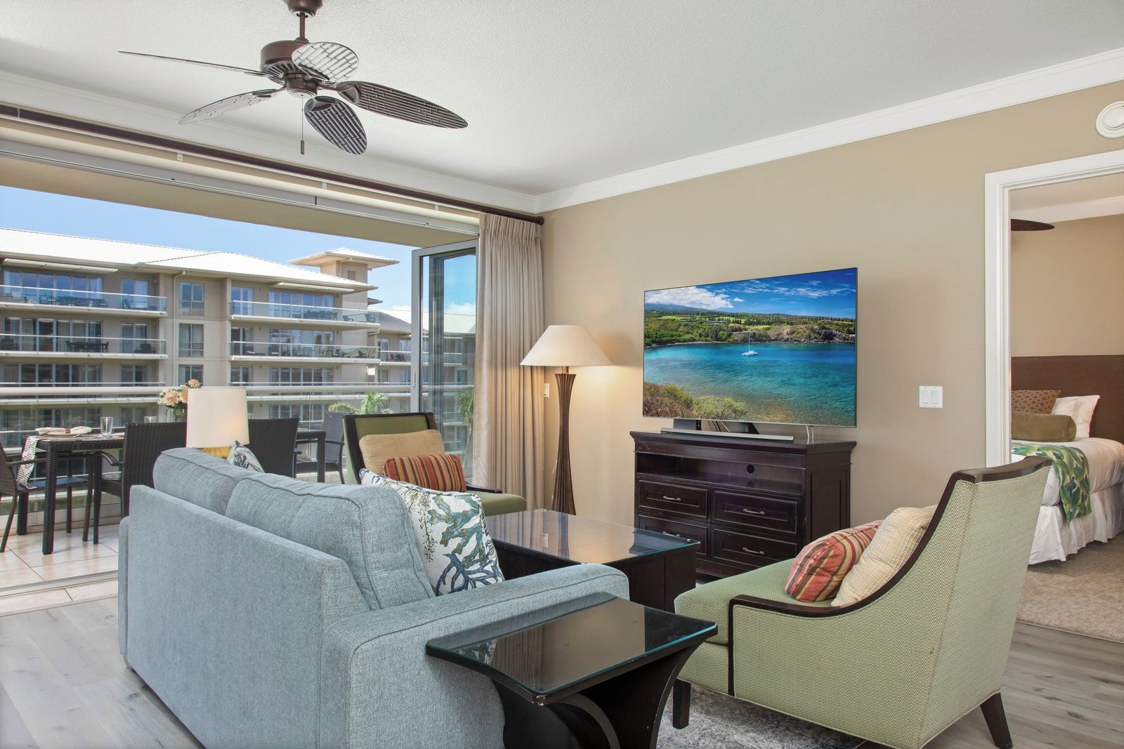 Une chambre d’hôtel avec un balcon, une télévision, un canapé, un fauteuil et un coin repas comprenant une table et des chaises.