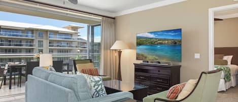 Une chambre d’hôtel avec un balcon, une télévision, un canapé, un fauteuil et un coin repas comprenant une table et des chaises.