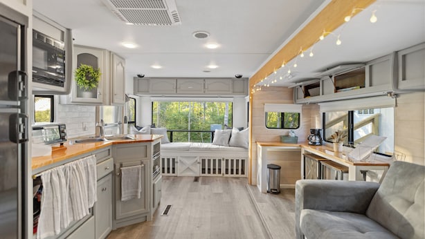 Un intérieur de camping-car compact comprenant un coin cuisine, un espace salon et une fenêtre offrant une vue sur la verdure.
