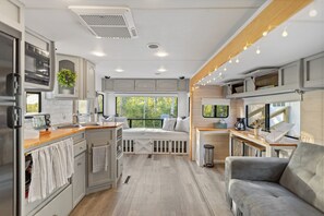 Interior compacto de una autocaravana con kitchenette, zona de estar y ventana que ofrece vistas al verdor.
