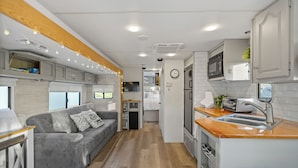 Un intérieur de camping-car compact comprenant un coin cuisine, un canapé gris et un plafond en bois.