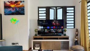 Olohuone, jossa on televisio, sohva, sohvapöytä ja ikkuna, jossa on sälekaihtimet.