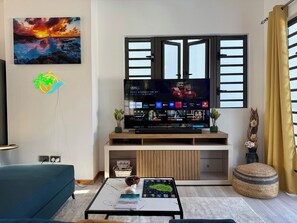 A living room with a TV, a sofa, a coffee table, and a window with blinds.