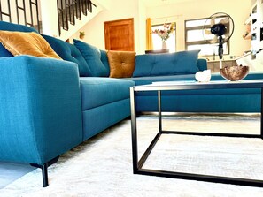 Un salon avec un canapé bleu, une table basse et un escalier en arrière-plan.