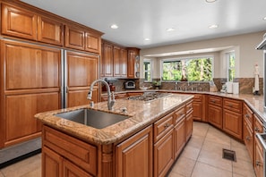 A kitchen with wooden cabinets, a granite countertop, stainless steel appliances, and a window providing a view of greenery. - Grand Oriole Estate - Luxury Estate | Pool, Hot Tub, Game Room (Big Bear Lake)