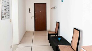 Un couloir avec une porte en bois, deux fauteuils en osier, une petite table et un luminaire fixé au mur.