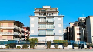 Un immeuble résidentiel à plusieurs étages, doté de balcons, d’une entrée principale et surplombant un ciel d’un bleu éclatant.