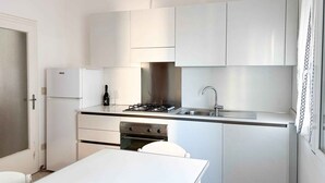 Une cuisine de taille réduite, avec des meubles blancs, une cuisinière à gaz, un évier et un réfrigérateur.