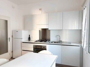 A compact kitchen with white cabinets, a gas stove, a sink, and a refrigerator. - Holiday apartment with air conditioning (Lido di Jesolo)