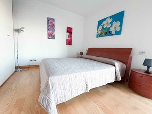 A bedroom with a bed, a nightstand, a lamp, and wall art. - Holiday apartment with balcony (Jesolo)