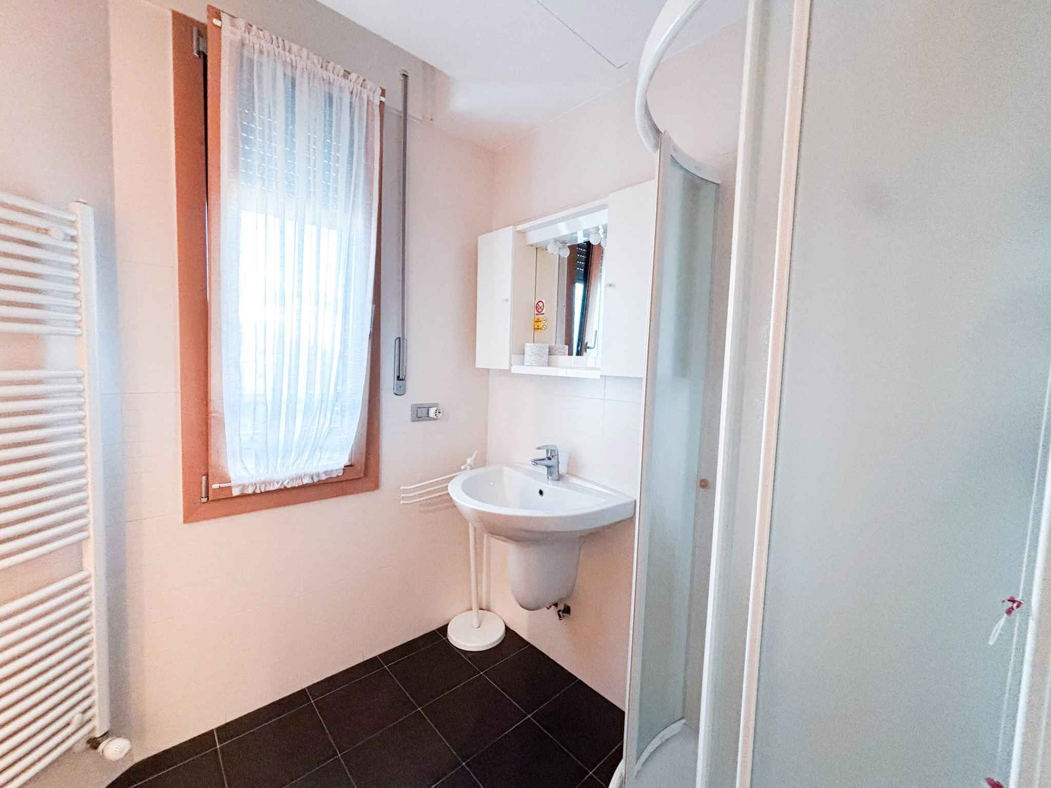 Een badkamer met een wit wastafel, een spiegel, een raam met dunne gordijnen en een radiator.