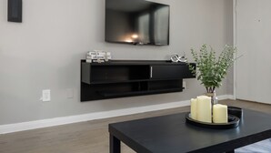 Un salon moderne avec un téléviseur à écran plat fixé au mur, un meuble noir pour appareils électroniques en dessous, et une table agrémentée de bougies et d’une plante.