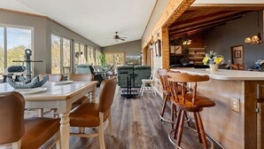 A spacious dining area with a high ceiling, large windows, and a bar area with stools. - Lakefront, Private Dock, Water Toys, Sunset Views! (Jefferson City)