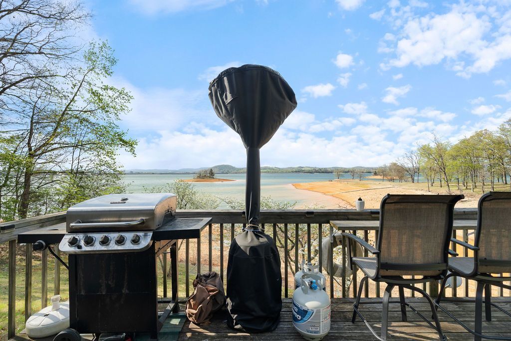 A barbecue grill, chairs, and a gas tank on a deck with a view of a beach and water.