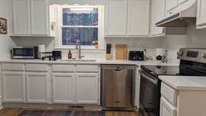 A modern kitchen with white cabinets, stainless steel appliances, and a window with a view of trees. - Adorable home between Duke and UNC alongside trails (Durham)