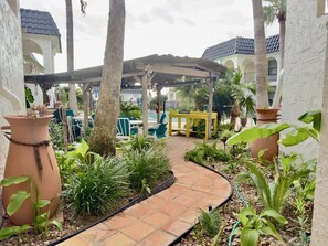 A covered outdoor area with a curved pathway, potted plants, and a yellow bench. - Starfish Stay | Tranquil Pool | Directly Across From Beach (Corpus Christi)