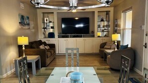 A dining area with a glass table, chairs, a chandelier, a TV, and a sofa. - Starfish Stay | Tranquil Pool | Directly Across From Beach (Corpus Christi)