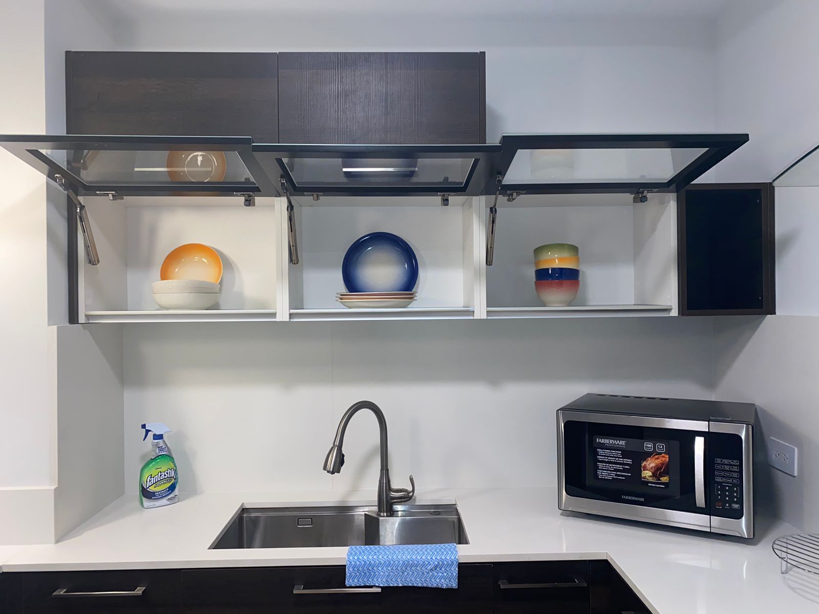 Una cocina con microondas integrado, pileta de acero inoxidable y estantes con vajilla.