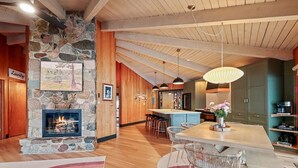 A spacious kitchen with a central island, a stone fireplace, and a dining area with a colorful rug. - Lakefront Retreat with Sandy Beach, Swim Area & Relaxing Lakeside Seating! (Eagle River)