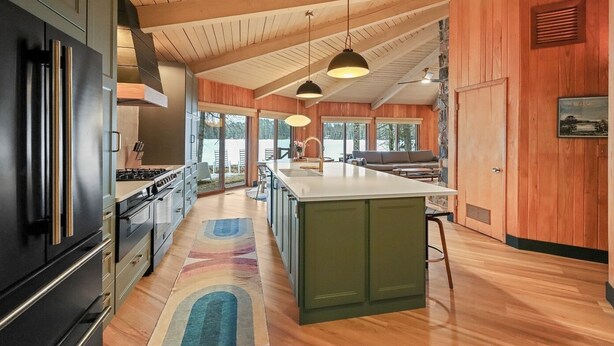 A modern kitchen with a large island, pendant lighting, and wooden paneling. - Lakefront Retreat with Sandy Beach, Swim Area & Relaxing Lakeside Seating! (Eagle River)