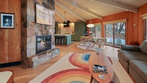 A cozy living room with a stone fireplace, wooden ceiling, and a dining area with a large window. - Lakefront Retreat with Sandy Beach, Swim Area & Relaxing Lakeside Seating! (Eagle River)
