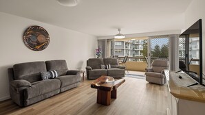 A modern living room with a sofa set, a wooden coffee table, and a dining area with a table and chairs. - Coastal Comfort with Ocean Views  (Burleigh Heads)