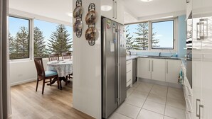 A modern kitchen with a large refrigerator, white cabinets, and a dining area with a table and chairs. - Coastal Comfort with Ocean Views  (Burleigh Heads)