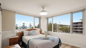 A bedroom with a bed, bedside table, lamp, and large windows offering a city view. - Coastal Comfort with Ocean Views  (Burleigh Heads)