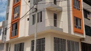 Un edificio de varios pisos con balcones, una tapa de alcantarilla y un letrero en la planta baja.