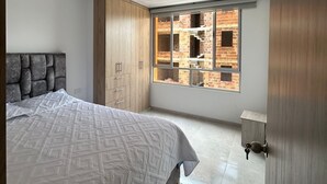 Un dormitorio con cama, armario de madera y ventana con vista a un edificio de ladrillo.