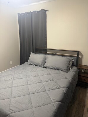 Ein Bett mit einer gesteppten grauen Decke, einem Holz-Kopfteil und einem Nachttisch mit einer Schublade.