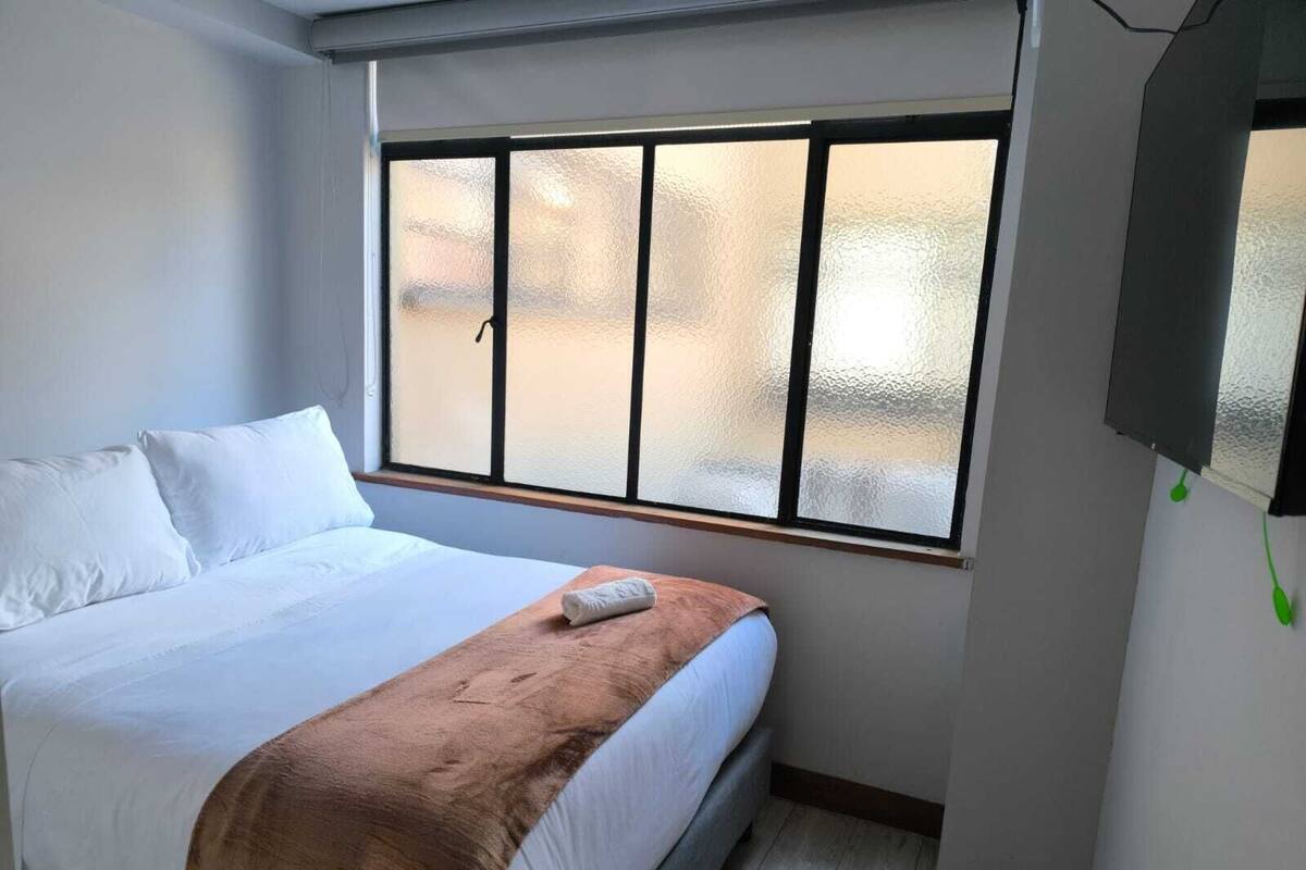 A single bed with white linens, a brown throw blanket, and a window with frosted glass.
