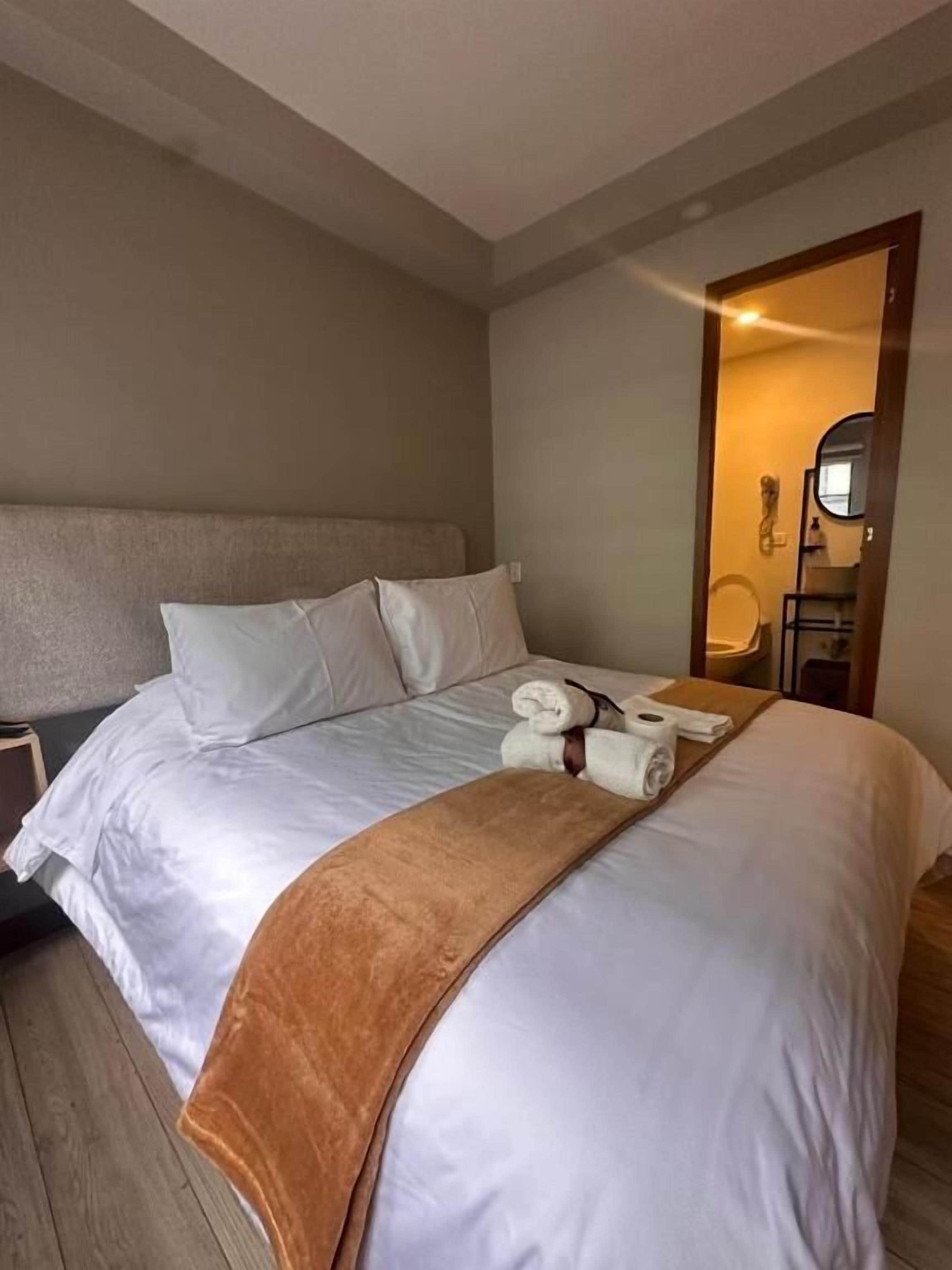 Habitación de hotel con una cama grande, piso de madera, un espejo y un baño visible a través de una puerta abierta.