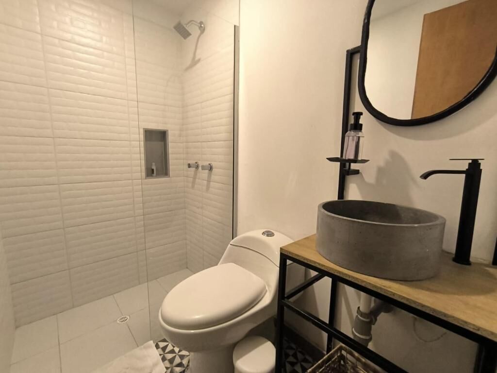 Un bagno moderno con un water bianco, una doccia e un lavandino con una vasca rotonda.