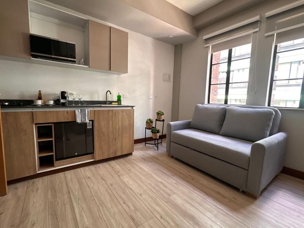 Een moderne keuken met inbouwapparatuur, een grijze bank en een raam dat voor natuurlijk licht zorgt.