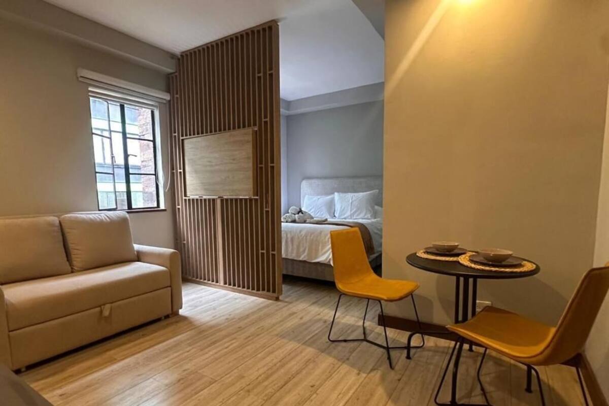 A modern room with a sofa, two chairs, a small table, a bed, and a window.