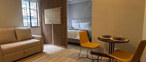 A modern room with a sofa, two chairs, a small table, a bed, and a window.