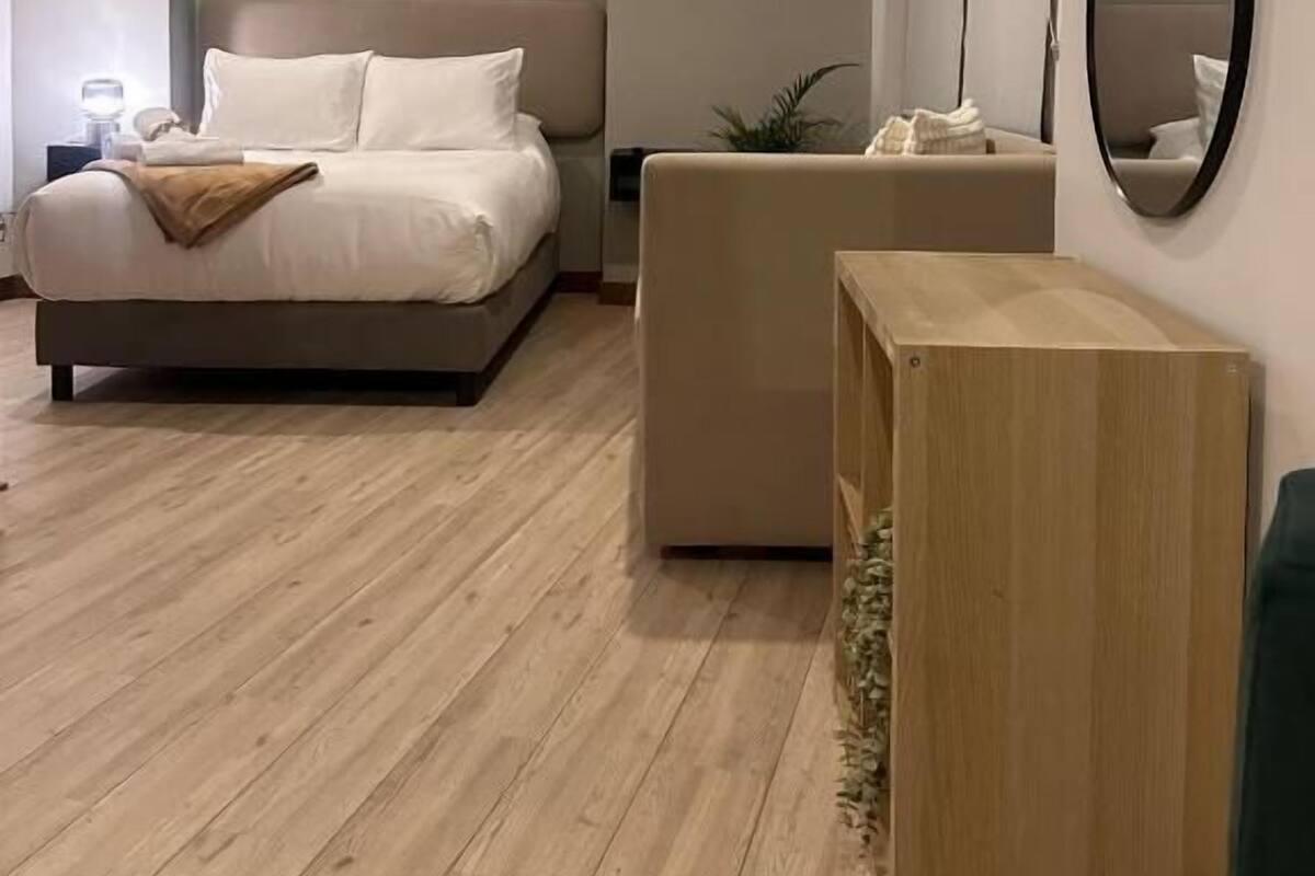 A modern bedroom with a bed, bedside table, and a mirror.
