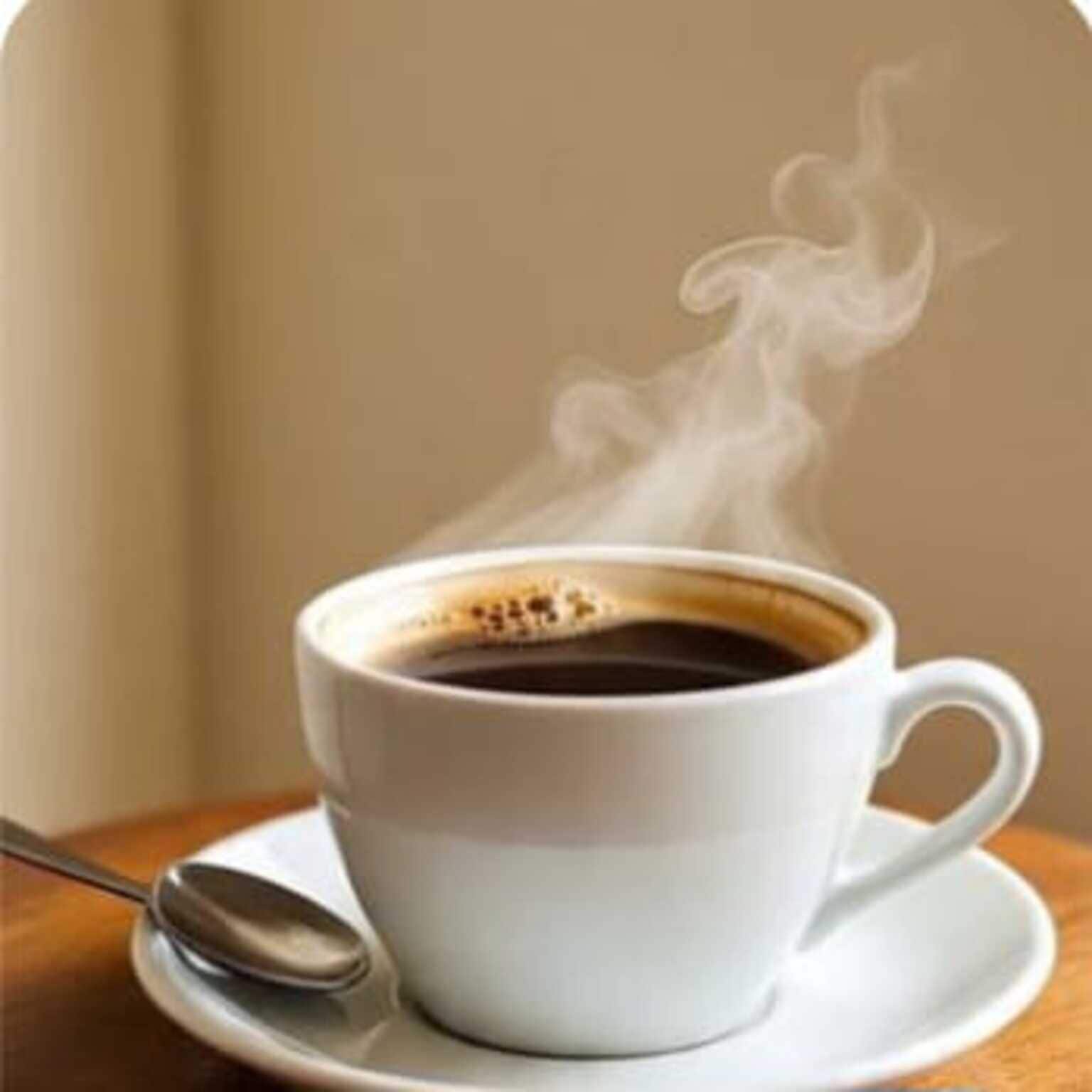 En hvid kaffekop med damp, en ske og en underkop på et træbord.
