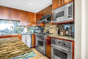 A modern kitchen with wooden cabinets, stainless steel appliances, and a stone backsplash. - 3 Honua Kai Villas | Ocean Front | Sleeps 22 | Free Car w/ 6+ Nights | ML-3188 (Lahaina)