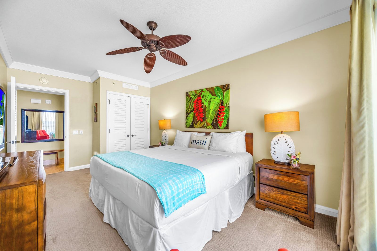 A hotel room with a bed, a ceiling fan, a nightstand with a lamp, a painting, and a door.