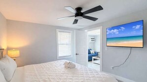 Quarto com cama, ventilador de teto, televisão e porta para outro cômodo.