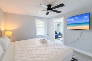 Ein Schlafzimmer mit einem Bett, einem Deckenventilator, einem Fernseher und einer Tür zu einem anderen Raum.